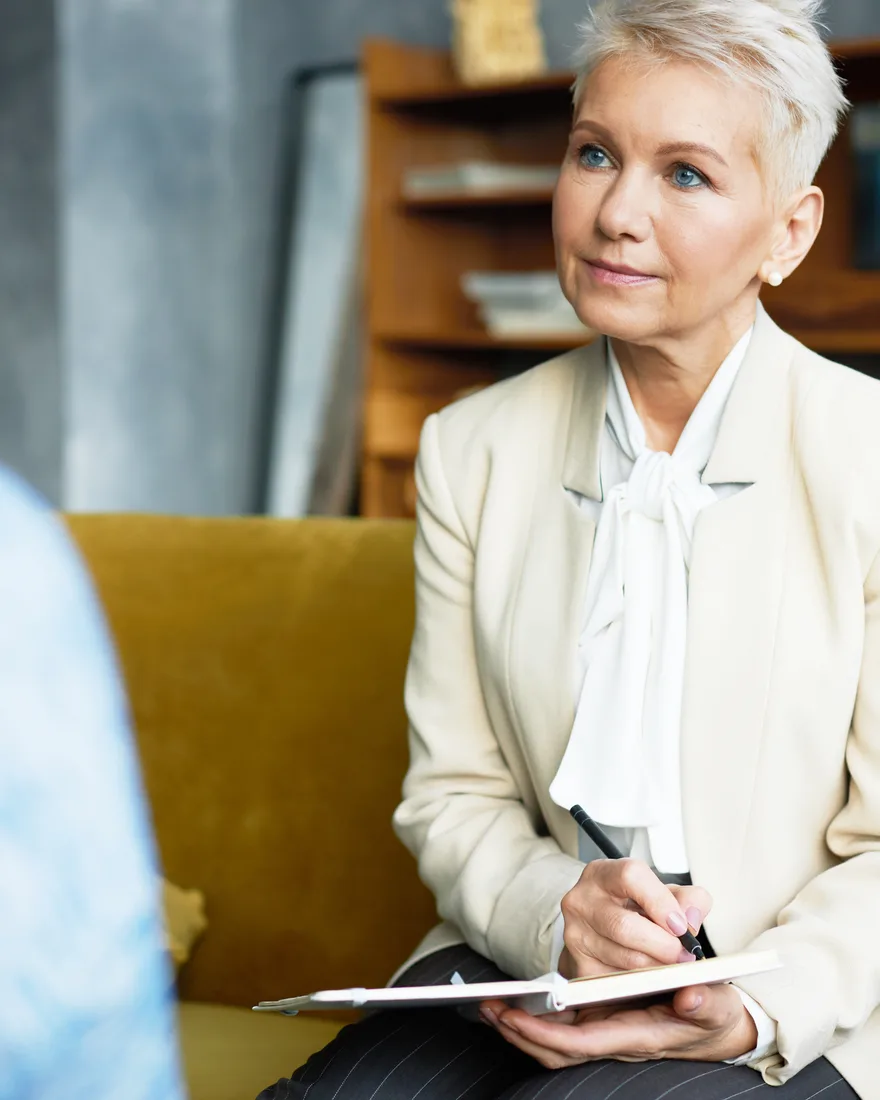 An experienced coach with silver hair listens attentively and takes notes during a coaching session.